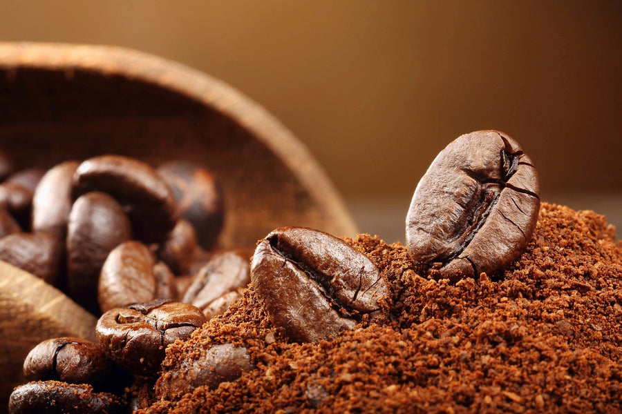 The Ground Coffee and Beans Wall Mural showcases a close-up of a textured coffee bean amidst ground coffee, while whole beans spill from a wooden scoop in the backdrop. Warm lighting enhances the rich brown hues, creating a cozy and aromatic atmosphere.