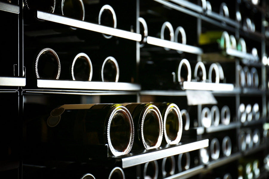 Cylindrical wine bottles are stored horizontally on black metal racks in a dim wine cellar. Deposit photo’s Modern Wine Rack Wall Mural, featuring vineyard scenes, adds charm to the atmosphere while soft lighting highlights the bottle necks and surfaces.