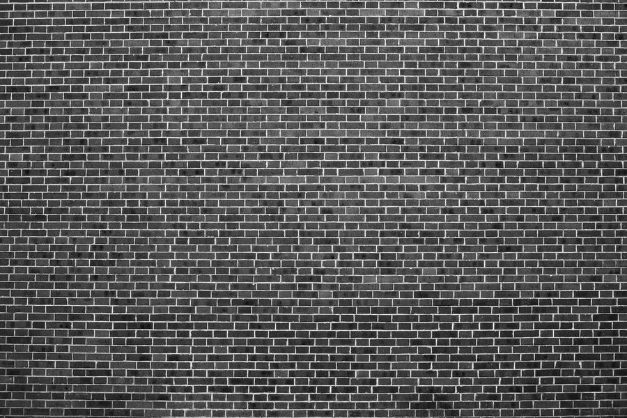 A close-up of the Monochrome Brick Pattern Wall Mural featuring dark gray bricks in a uniform, horizontal layout. This peel and stick removable wallpaper offers a modern look with light-colored mortar between each brick.