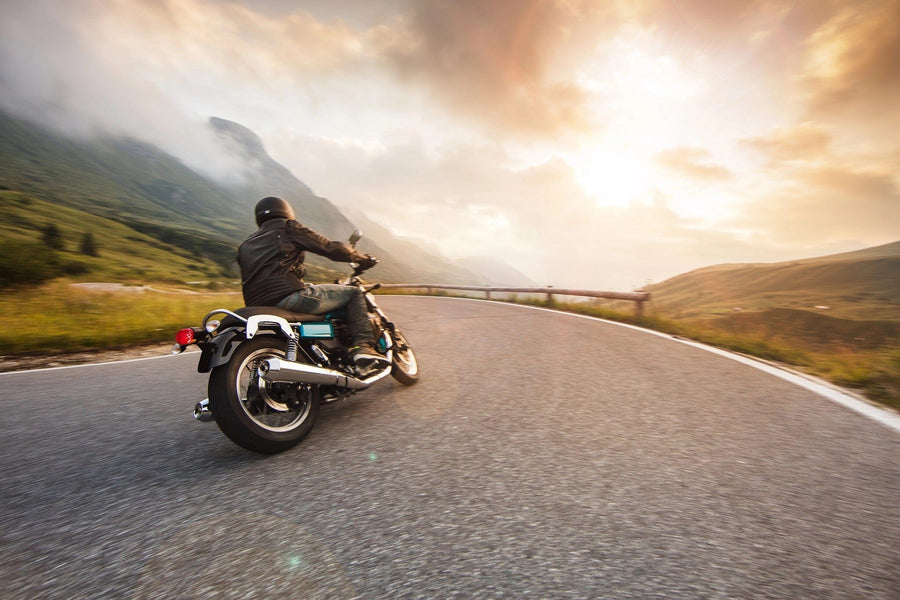 A motorcyclist in a black helmet rides a winding mountain road at dawn, with the sun illuminating misty peaks and lush green hills, capturing the essence of freedom and adventure just like the Mountain Road Escape Wall Mural.