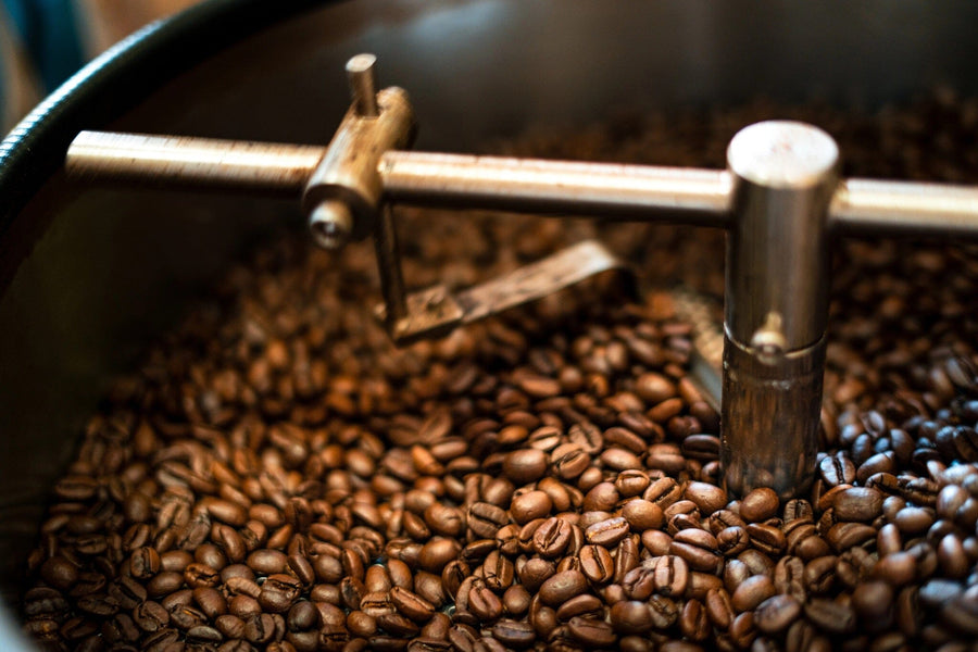 A close-up of roasted coffee beans in a metal roaster, featured on the Perfect Batch Wall Mural. Ideal as custom printed or removable wallpaper to add warmth and texture to any space.