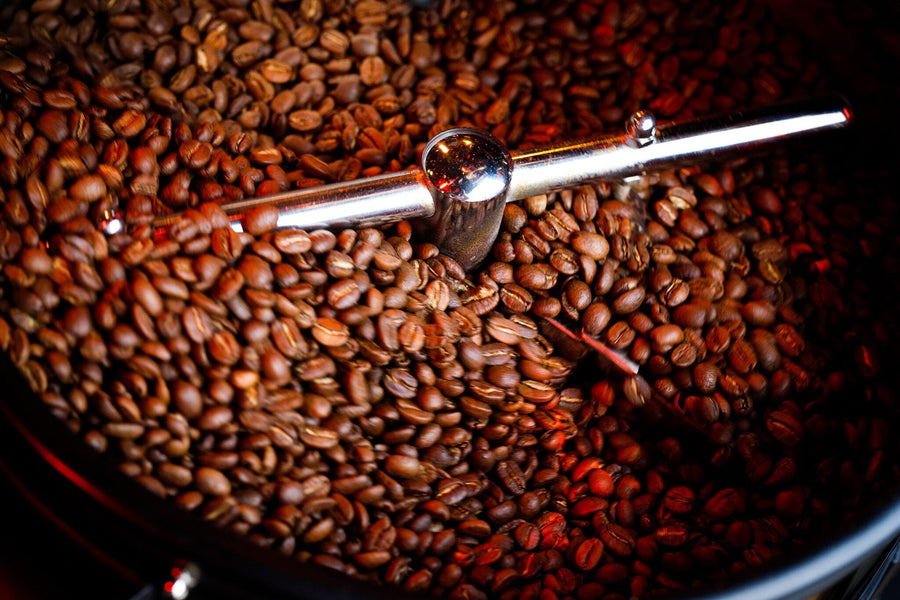 Close-up of roasted coffee beans swirling in a metal roasting machine, captured in warm, rich tones—Perfect Roast Wall Mural brings café vibes to your space as a custom printed or peel and stick mural.
