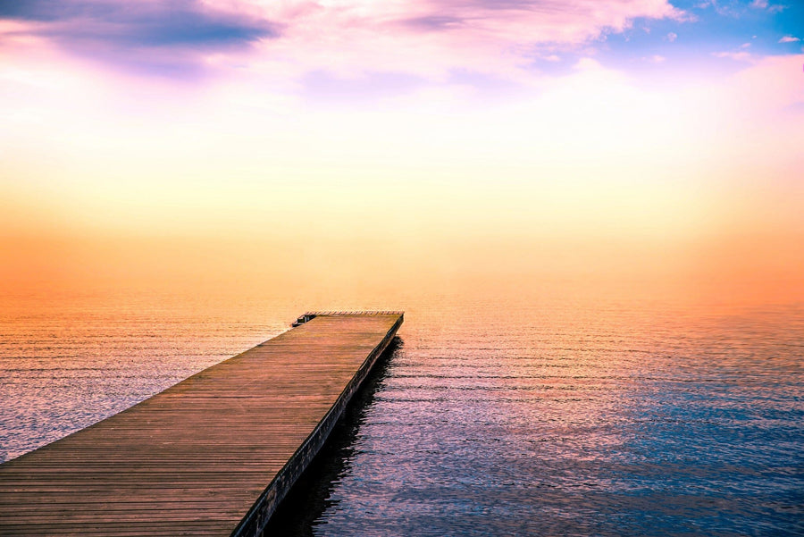 A wooden pier stretches into the tranquil sea, mirroring the sunrise's pink and orange hues, with the higher sky transitioning to gentle pink and purple tones—akin to the serene beauty depicted in Deposit Photo's "Pier in the Sea" wall mural.