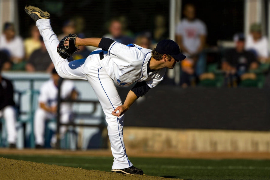 A pitcher in a white uniform and navy cap finishes his pitch on the mound, sunlight highlighting his form—captured in the Baseball 4 Wall Mural, perfect for adding stadium excitement to any room.