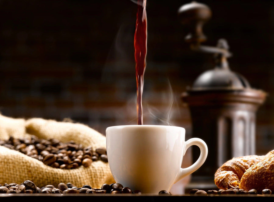 Fresh coffee steams in a white cup surrounded by beans, with a vintage grinder in the background, and a croissant nearby. This cozy breakfast scene is perfect for kitchens featuring the Coffee 1 Wall Mural by photo.