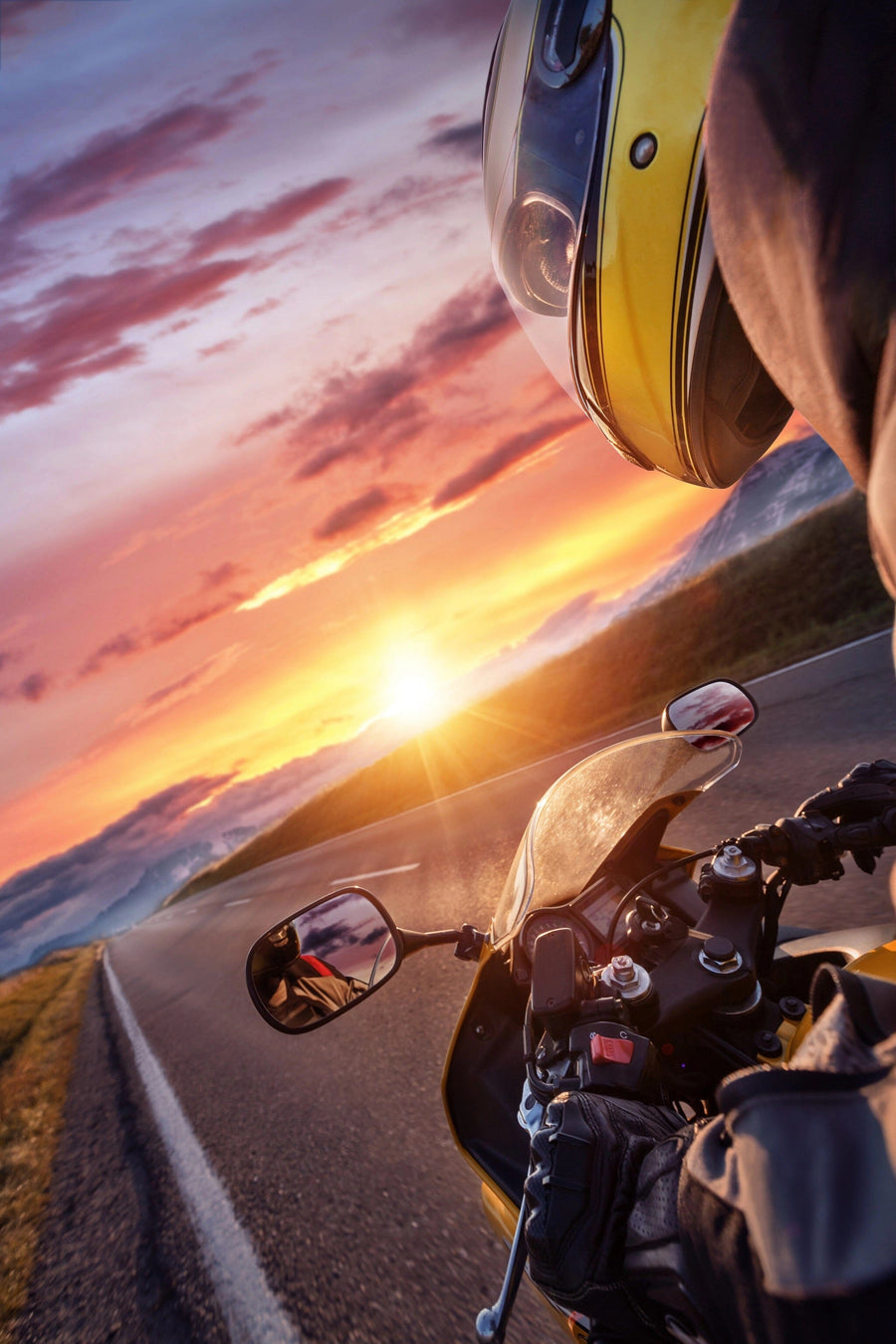 Wearing a yellow helmet, a motorcyclist navigates a winding road at sunset, as the sky resembles the vibrant hues of the Rider at Sunset Wall Mural by  photo. The sun dips low, capturing both motion and scenic beauty.