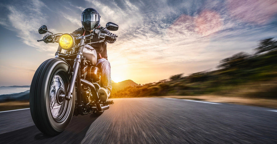 A motorcyclist in a black helmet rides along a winding road, their headlight glowing, echoing the adventurous spirit of the Sunset Ride Rush Wall Mural, showcasing vibrant sunset hills and capturing the dynamic beauty of the open road.