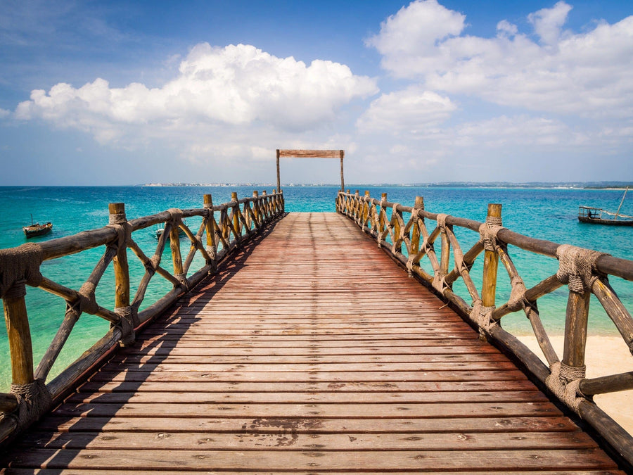 The Pier 9 Wall Mural showcases a wooden pier over turquoise waters leading to a square frame, with fluffy clouds in a bright blue sky reflecting off the serene scene. Boats dot the horizon, logs, and rope railings adding rustic charm—like entering your own custom-printed paradise.