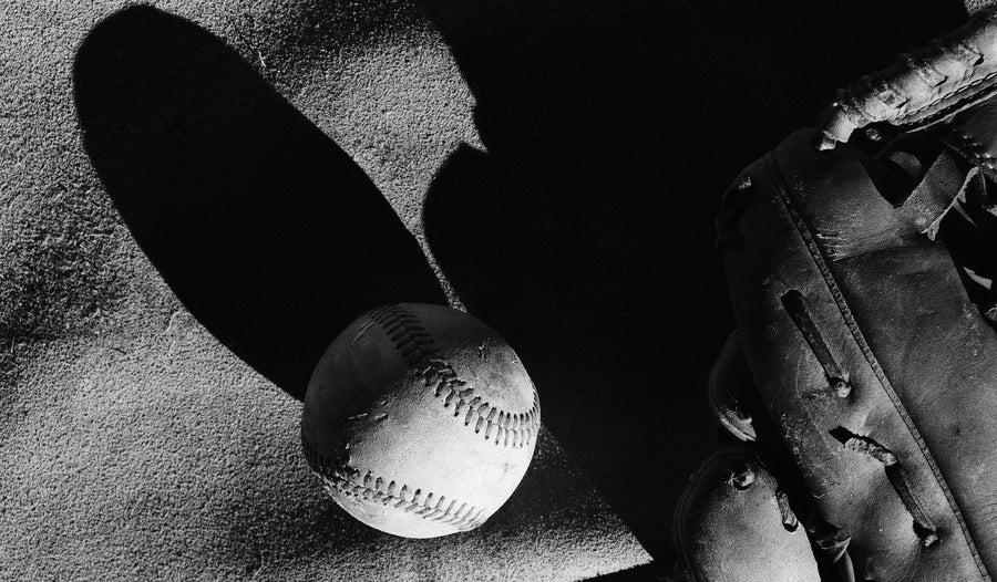 The Vintage Baseball Wall Mural features a black and white image of a worn glove and baseball on textured ground. Dramatic shadows add contrast, making this peel and stick mural ideal for any baseball fan’s space.