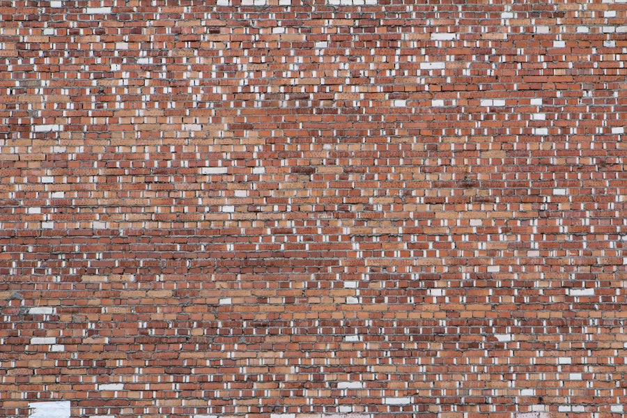 A modern living and dining area features a Mismatched Bricks Wall Mural, blue armchairs, green sofa, round coffee table, wooden dining table for six, pendant lights, rugs, hardwood floors, and a kitchen with white cabinets in the background.