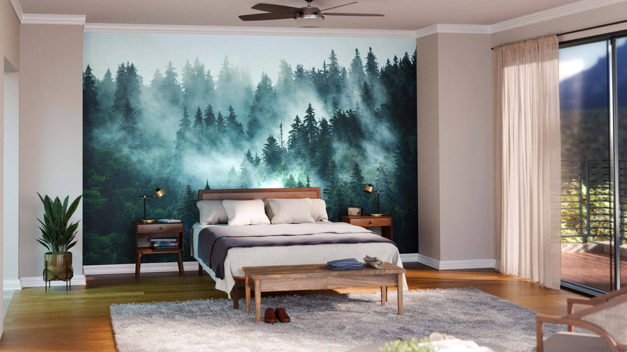 Modern living-dining space with wooden floors, a gray sofa, teal armchairs, the Misty Foggy Forest Wall Mural, a long dark dining table with chairs, spherical pendant lights, plants, and a visible kitchen in the background.