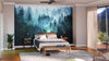 A modern bedroom is anchored by the Misty Mountain Way Wall Mural behind a wooden bed. Neutral walls, nightstands with lamps, a cushioned bench, plant, sheer curtains, and a light gray rug complete this serene space.