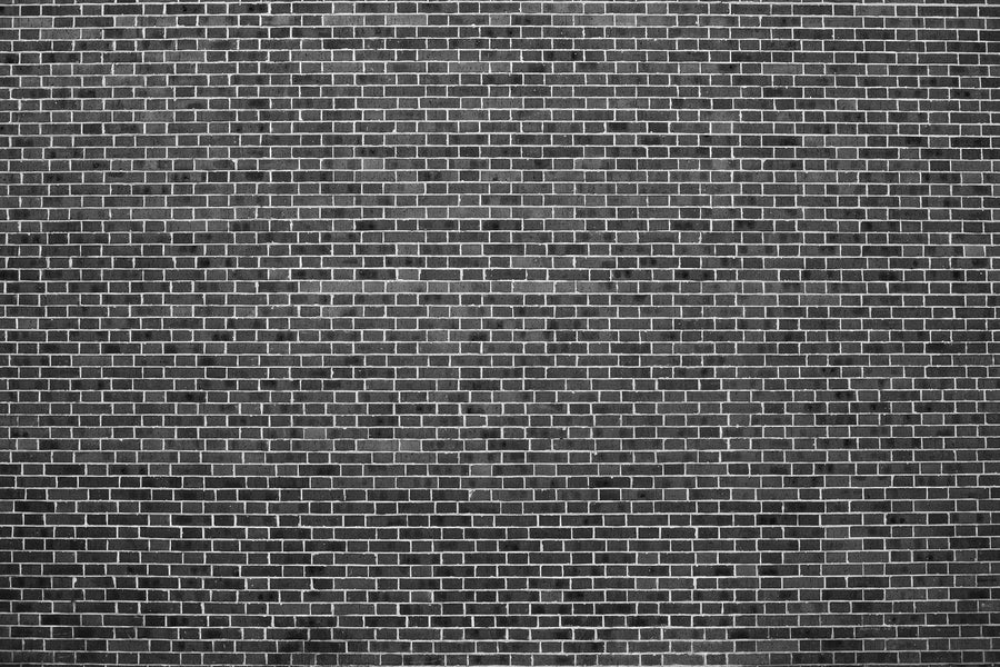 A modern living and dining area features teal armchairs, a gray sofa, a wooden coffee table, and a dark accent wall highlighted by the Monochrome Brick Pattern Wall Mural, with houseplants and an open kitchen with yellow cabinets in the background.
