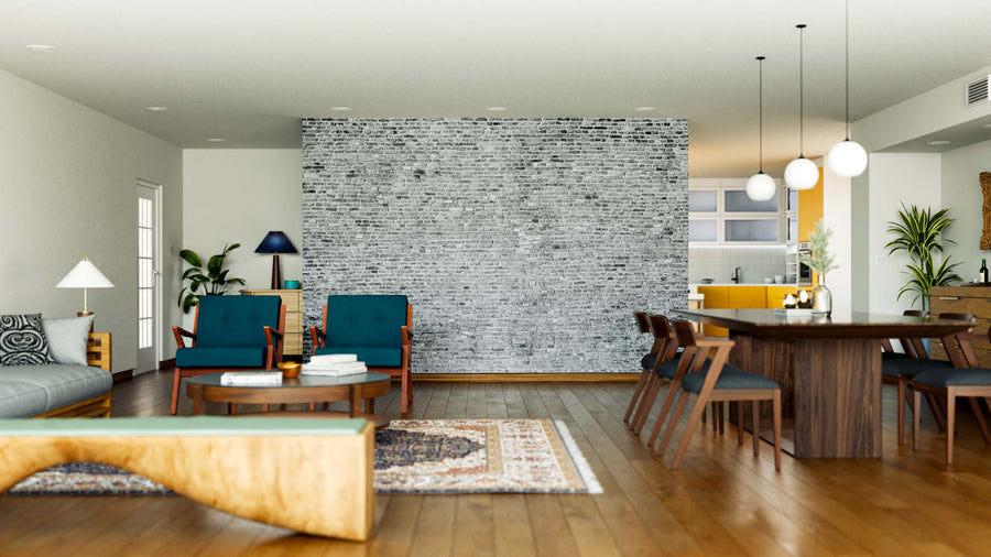 Modern open-plan living and dining area with wooden floors, blue armchairs, a Monochrome Brick Wall Wall Mural as an accent, sofa, rugs, long wooden dining table with chairs, pendant lights, kitchen in the background, and plants.