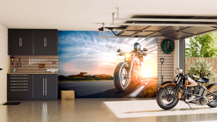 A modern garage with sleek black cabinets, organized tools, and a vintage motorcycle features the "Cruising into Sunset Wall Mural" on the back wall, adding dynamic energy to the clean, well-lit space.