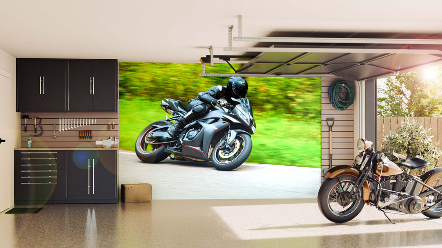 A modern garage with dark cabinets, organized tools, a classic motorcycle on the right, and a large Motorbike Racing Wall Mural showing a rider in black gear speeding on a green, blurred road. Sunlight streams through an open door.