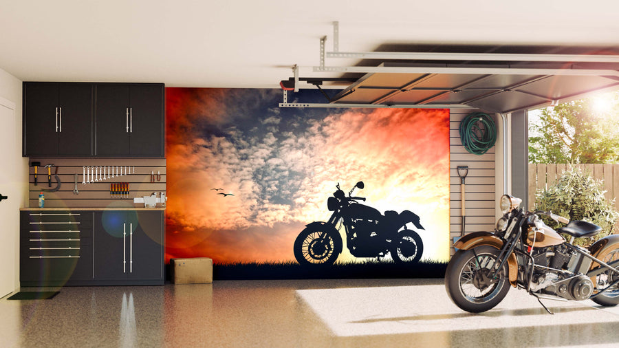 A modern garage with black cabinets, organized tools, and a motorcycle on a shiny floor. The back wall features the Motorcycle Wall Mural—a stunning motorcycle silhouette at sunset. A garden hose hangs on the right wall.
