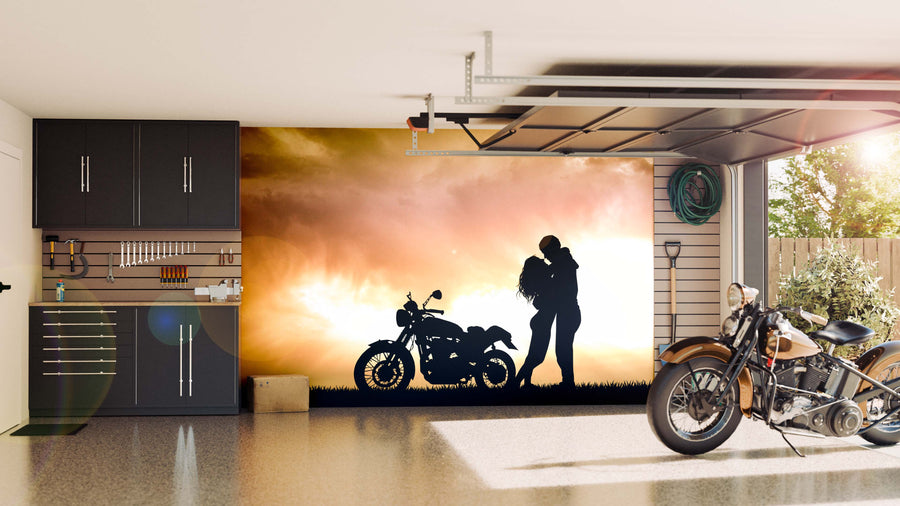 A tidy garage with dark cabinets, tools, and a classic motorcycle. On the back wall is the Motorcycle Couple Wall Mural—a black silhouette of a couple beside a motorcycle at sunset. Sunlight streams in from the open door.