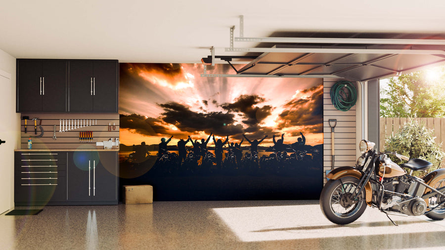 A modern garage with black cabinets, a tool rack, and a motorcycle. The back wall showcases the Motorcycle Group Wall Mural featuring cheering people at sunset. Sunlight fills the clean, organized space.