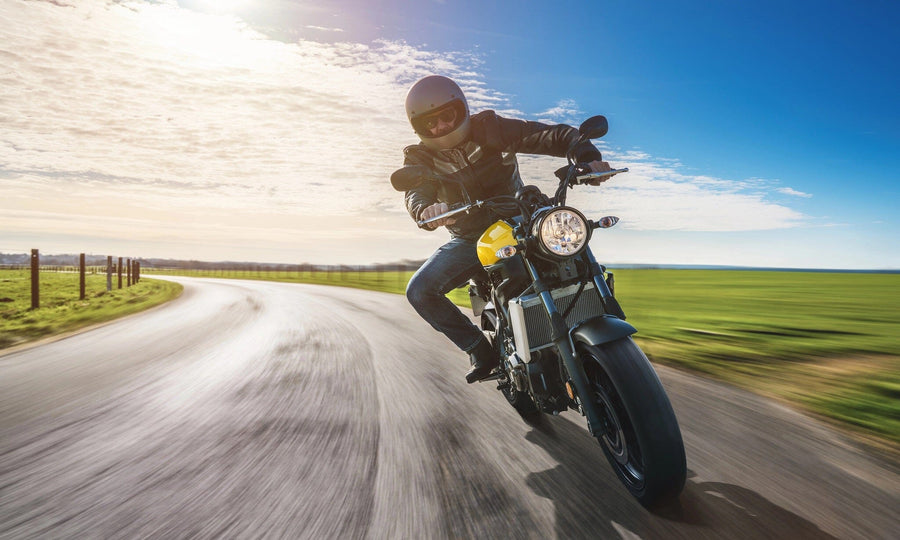 A tidy garage features gray cabinets, tools arranged on wall racks, a motorcycle on a speckled floor, and a large Motorcycle Rider Adventure Wall Mural showing someone riding down a sunny rural road as sunlight pours in through the open door.