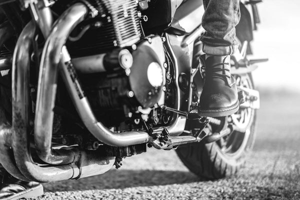 The "Motorcycle Rider Boot Wall Mural" by Deposit Photo captures the adventurous spirit with a black-and-white close-up of a motorcycle rider's boot on the footrest. The detailed engine and exhaust pipes cast shadows, and the blurred road background suggests motion or readiness to ride.