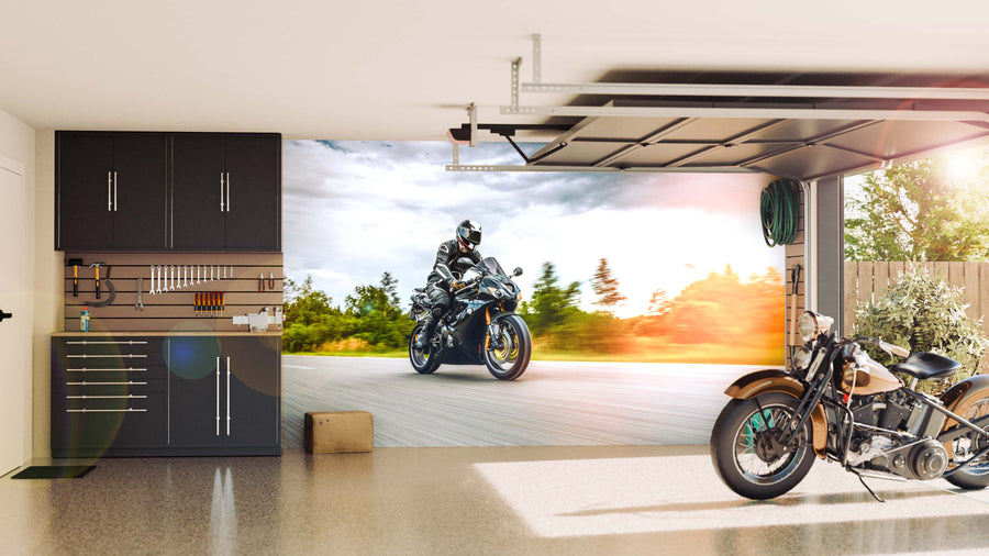 A modern garage with sleek black cabinets and a tool rack on the left. The back wall features the Riding into Motion Wall Mural showing a speeding motorcyclist. A vintage motorcycle rests by an open door with greenery outside.
