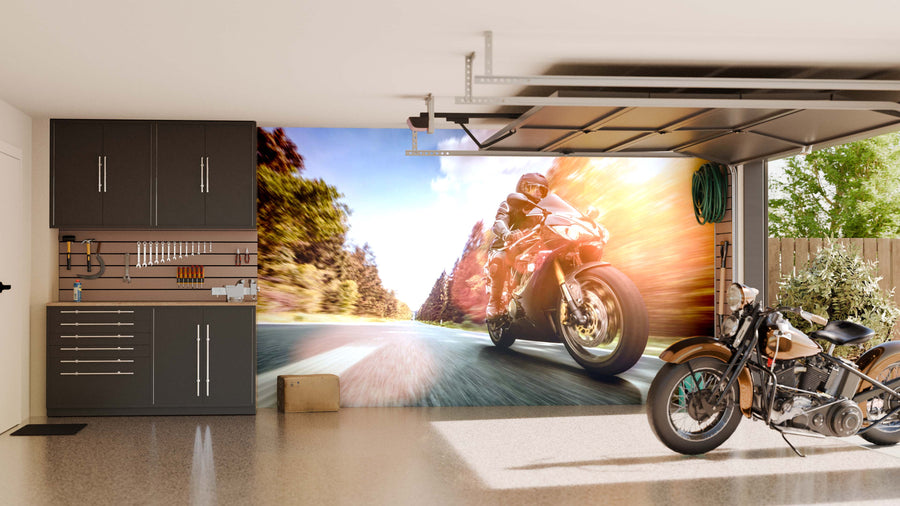 A modern garage with gray cabinets, organized tools, and a classic motorcycle. The Road Rush Wall Mural on the back wall shows a motorcyclist speeding down a scenic road, adding excitement and motion to the space.