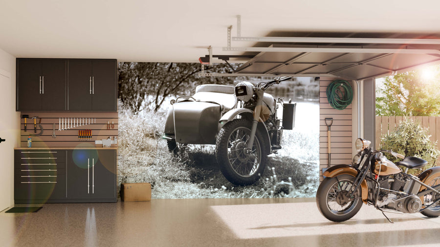 A modern garage with black cabinets, organized tools, and a vintage motorcycle. The back wall features the Vintage Sidecar Classic Wall Mural, showcasing an old motorcycle with a sidecar. Sunlight pours in from the open garage door.