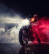 The "Motorcycle in Smoke Wall Mural" by Deposit photo features a dramatic scene of a motorcycle with bright headlights piercing through dense smoke, angled slightly. The rider's dark helmet is barely visible amidst red and white lights contrasting against the dark backdrop, while the road reflects the light.