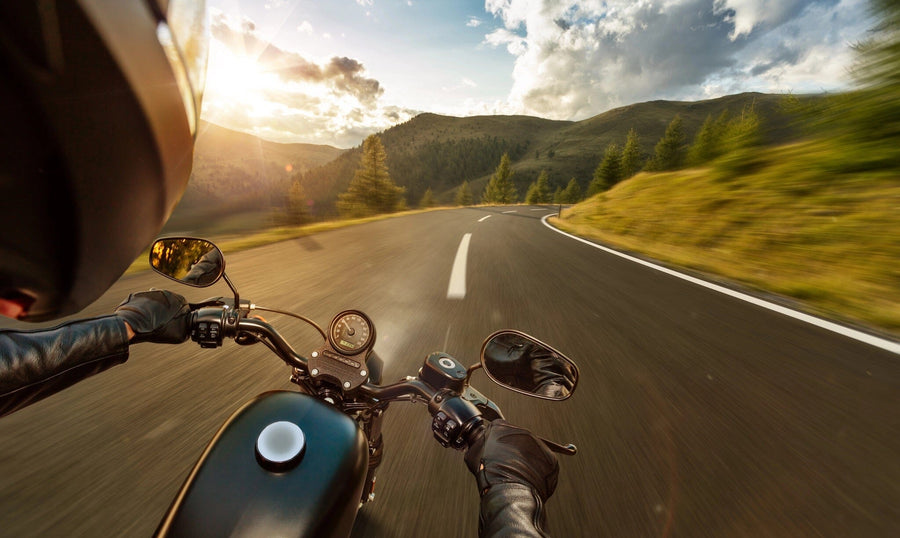 A sleek, organized garage with dark cabinets, tools, and a motorcycle. The back wall showcases the Mountain Drive Wall Mural—a peel and stick mural of a rider’s view on an open mountain road—illuminated by natural light from the open door.