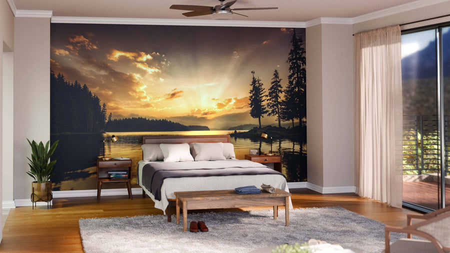 A cozy bedroom includes a large bed, wooden bench, and potted plant. Behind the bed, the Mountain Lake at Dawn Wall Mural creates a serene view. Sunlight streams through glass doors with sheer curtains on the right.