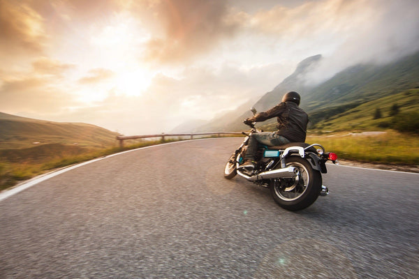 A motorcyclist in a black helmet rides a winding mountain road at dawn, with the sun illuminating misty peaks and lush green hills, capturing the essence of freedom and adventure just like the Mountain Road Escape Wall Mural.