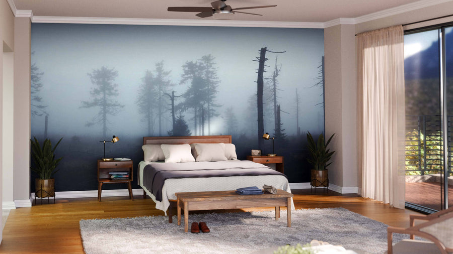A modern living and dining area with wooden floors features green armchairs, a gray sofa, a wooden bench, and is accented by the Mystical Silhouettes of Trees Wall Mural. The dining space has a dark wood table, chairs, globe pendant lights, and plants.