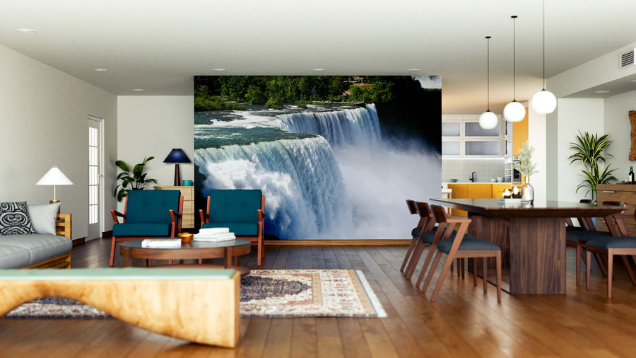 A spacious modern living and dining room features wooden floors, blue and wood furniture, hanging lights, and a Niagara Falls Landscape Wall Mural with lush greenery, creating a striking natural focal point in the stylish open space.