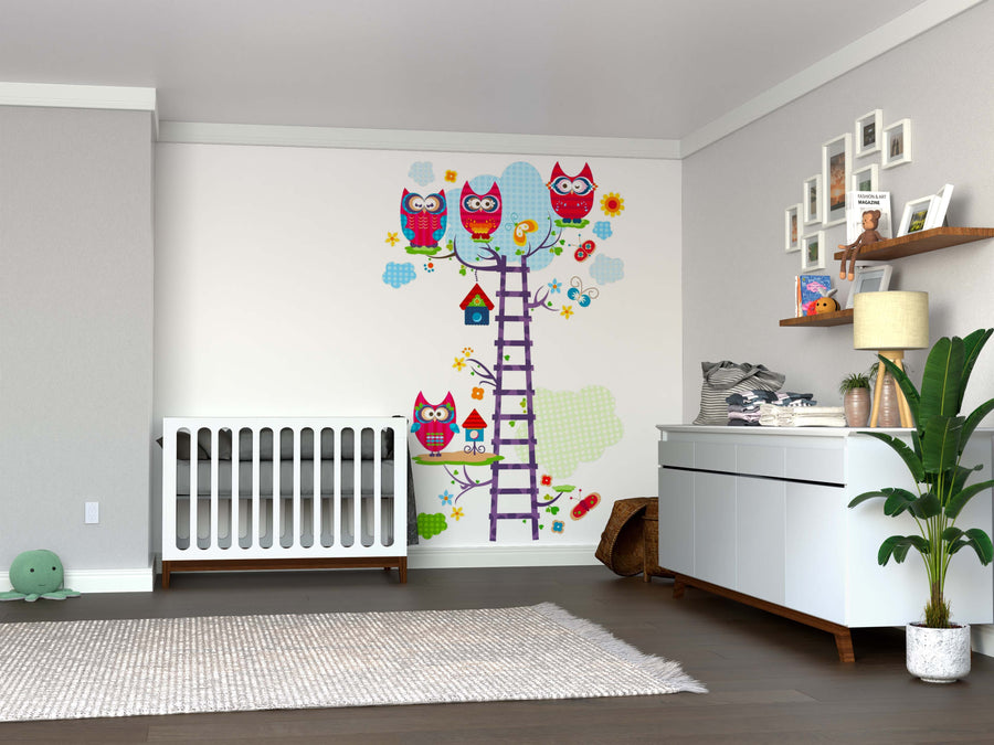 A cozy modern nursery featuring a white crib and dresser, potted plant, plush turtle, wicker basket, shelves, and a colorful "A Tree with Owls Wall Mural" that brightens the space along with a purple ladder and cheerful rug.