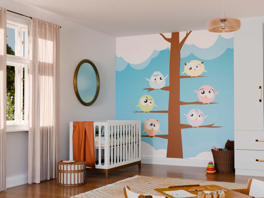 A nursery room with a white crib, orange blanket, round mirror, and wicker basket. The wall features the Barnyard Buddies Wall Mural—trees and cartoon birds on a blue sky. Sunlight filters through beige curtains; toys and books are scattered on the floor.