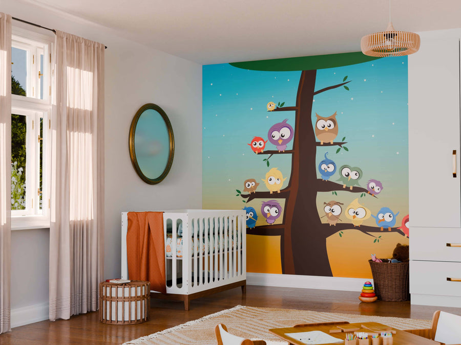A nursery with a white crib, orange blanket, round mirror, and sheer curtains features the Barnyard Buddies Wall Mural showing cartoon owls on a tree against a blue-orange sky. Toys and baskets are on the floor, with a woven light overhead.