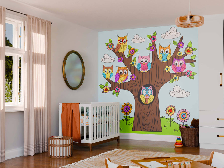 A cozy nursery features a crib, soft beige curtains, a rattan light fixture, and the Bright and Playful Owls Wall Mural with cartoon owls, flowers, and clouds. Wooden toys and storage baskets add charm to this cheerful room.