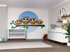 A nursery with a crib, dresser, plants, and shelves is brightened by the Brown Owls Wall Mural—four big-eyed cartoon owls on a branch in a blue circle—easy peel-and-stick decor for this calm, neutral-toned room.