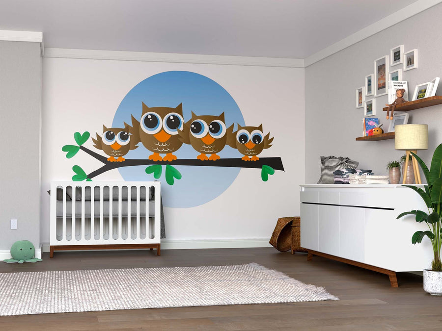 A nursery with a crib, dresser, plants, and shelves is brightened by the Brown Owls Wall Mural—four big-eyed cartoon owls on a branch in a blue circle—easy peel-and-stick decor for this calm, neutral-toned room.