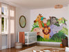 A bright nursery with a crib, wicker baskets, and a round mirror features the Cartoon Animals in the Jungle Wall Mural—peel and stick, showcasing a lion, elephant, zebra, giraffe, monkey, toucan, green leaves and grass.