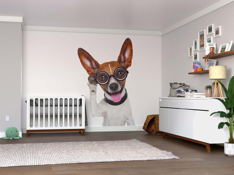 A modern nursery featuring the Clever Dog Wall Mural—a large peel and stick mural of a smiling dog in glasses—paired with a white crib, dresser, wall shelves, a plant, plush turtle toy, and soft rugs on hardwood floors.