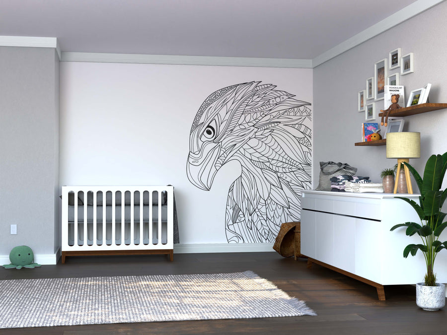 A modern nursery features a white crib, the Color My Eagle Wall Mural, a dresser with baskets and decor, framed photos, a potted plant, and a gray rug on dark wood floors. Neutral walls with crown molding complete the minimalist look.