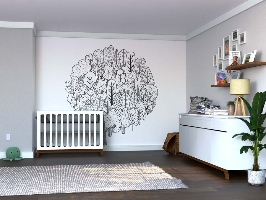 A modern nursery features a white crib, dresser, leafy plant, shelves with toys and books, a woven basket, plush turtle on a gray rug over dark wood floors, and whimsical black-and-white Color My Forest Wall Mural as removable wall art.