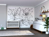 Modern nursery with a white crib, Color My Lily Wall Mural (peel and stick) featuring large outlined lilies, a white dresser with changing pad, toys and photos on the shelf, floor plant, lamp, gray rug, wood floors, and neutral walls.