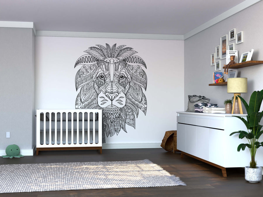 A modern nursery features the Color My Lion Wall Mural, a white crib, a dresser with a lamp and baby supplies, floating shelves with decor, a leafy plant, woven basket, and a soft rug on dark wood flooring.