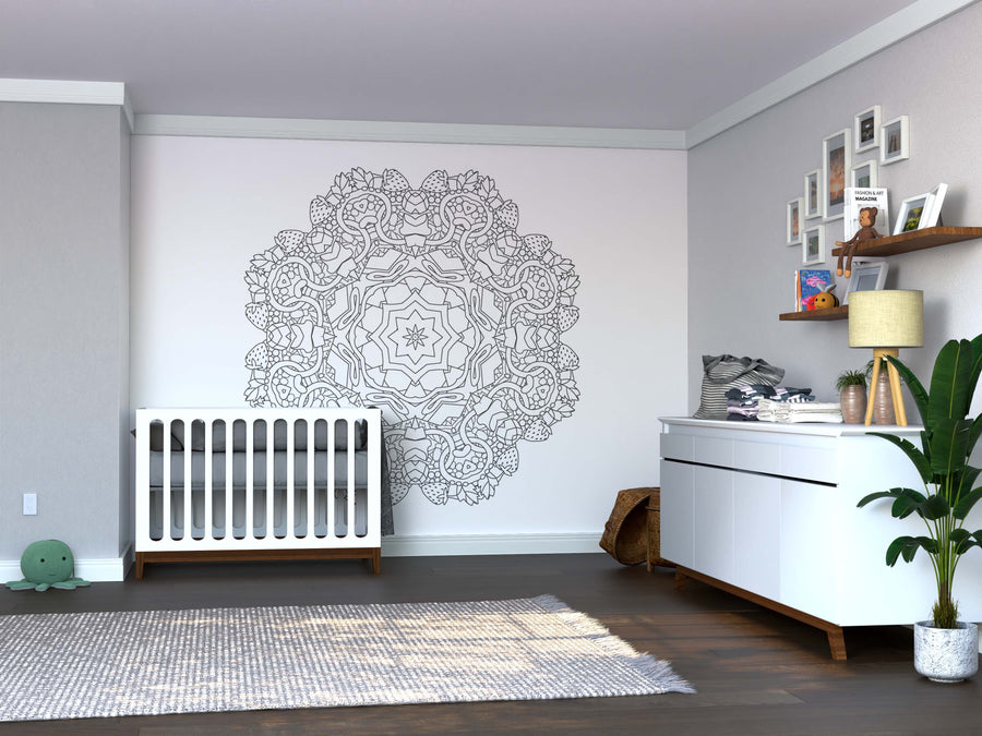 Modern nursery with a white crib and dresser on wooden floors. The Color My Strawberry Mandala Wall Mural adds vibrant detail, while plants, toys, baby supplies, framed photos, plush animals, and a light gray rug complete the space.