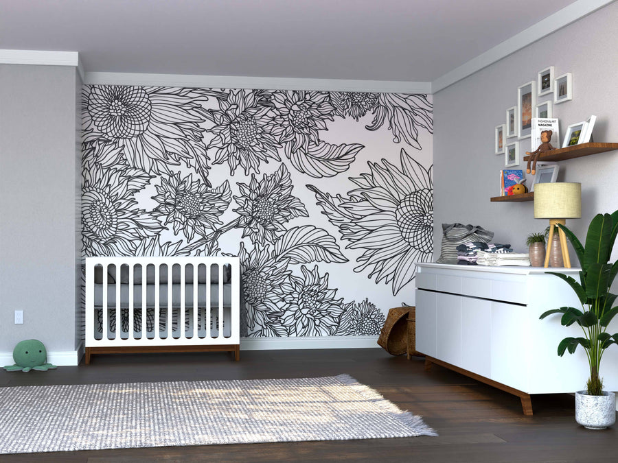 Modern nursery featuring the Color My Sunflower Wall Mural, white crib, dresser with lamp and decor, wall shelf with framed photos, wicker basket, plush toy on gray rug over dark wood flooring, and potted plant by the dresser.