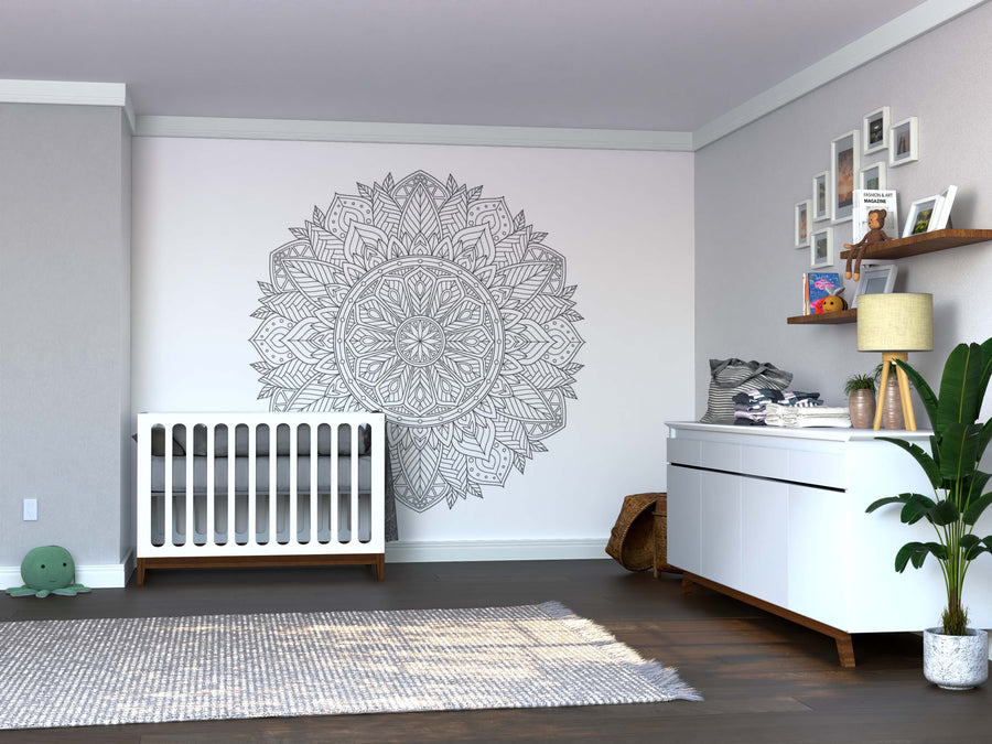Modern nursery with a white crib, Color My Wicker Mandala Wall Mural peel and stick on the wall, changing table with baby items, houseplants, framed photos on shelves, and gray rug on dark wood floors in a soft, neutral palette.