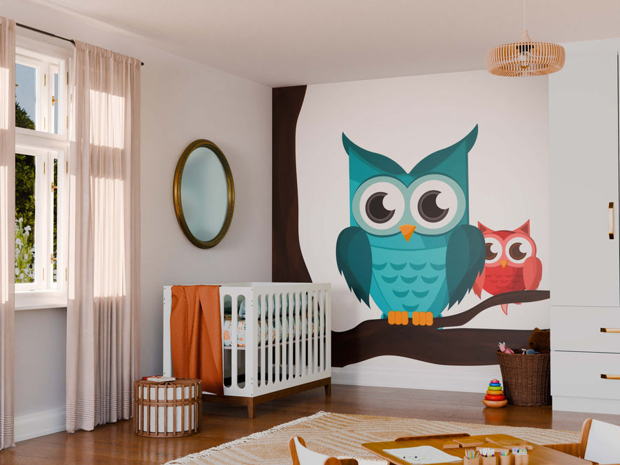 A cozy nursery features a white crib beside the Colorful Owls on Branch Wall Mural with teal and pink cartoon owls, plus light walls, beige curtains, a round mirror, wicker basket, toys, and soft natural light completing the space.